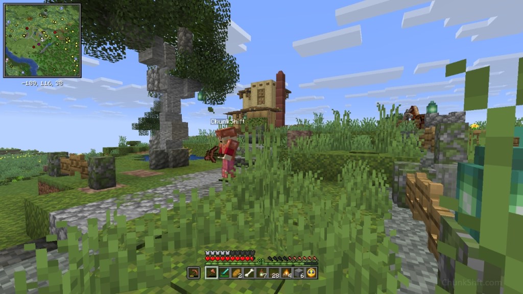 The player, covered in copper armour holds a copper pickaxe in one hand and an axe in the other. The player is standing on a cobble path surrounded by tall grass, a small custom tree and a fences.